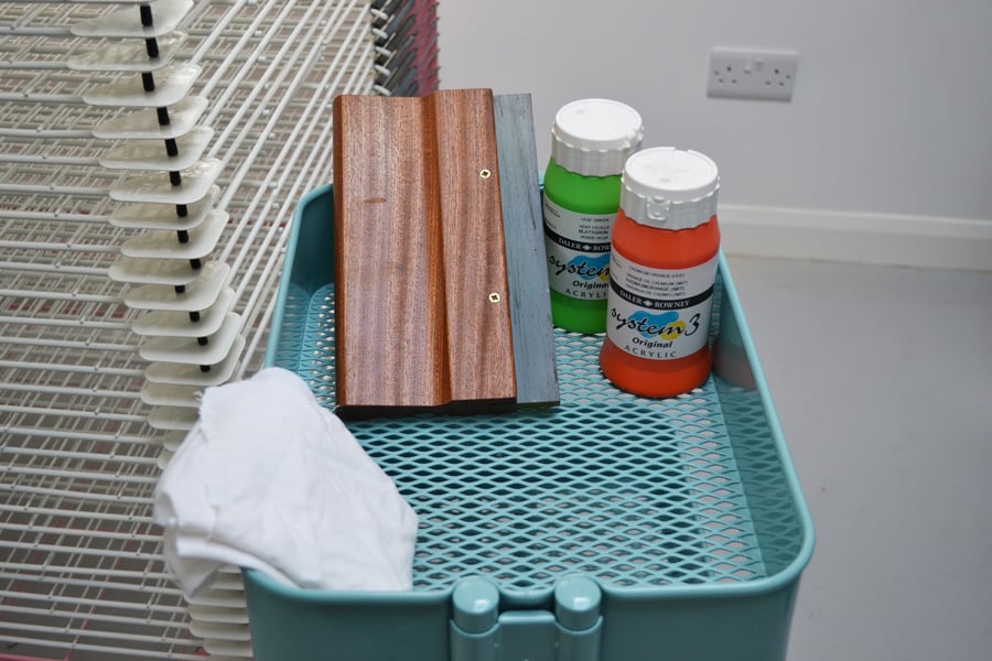 Dye Sublimation vs Screen Printing for Cosplay: Which One Wins? 2 A wooden squeegee and two bottles of water-based screen printing ink resting on a drying rack tray in a print studio.
